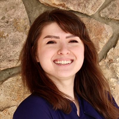 Chiropractor Evergreen CO Kristin Wodka Kristin Wodka smiling in front of stone wall wearing blue scrubs